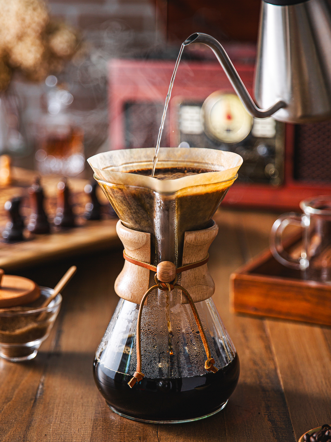 Brewing into a six-cup classic series coffeemaker, background is darker and sophisticated, a chess board, record player in the background 