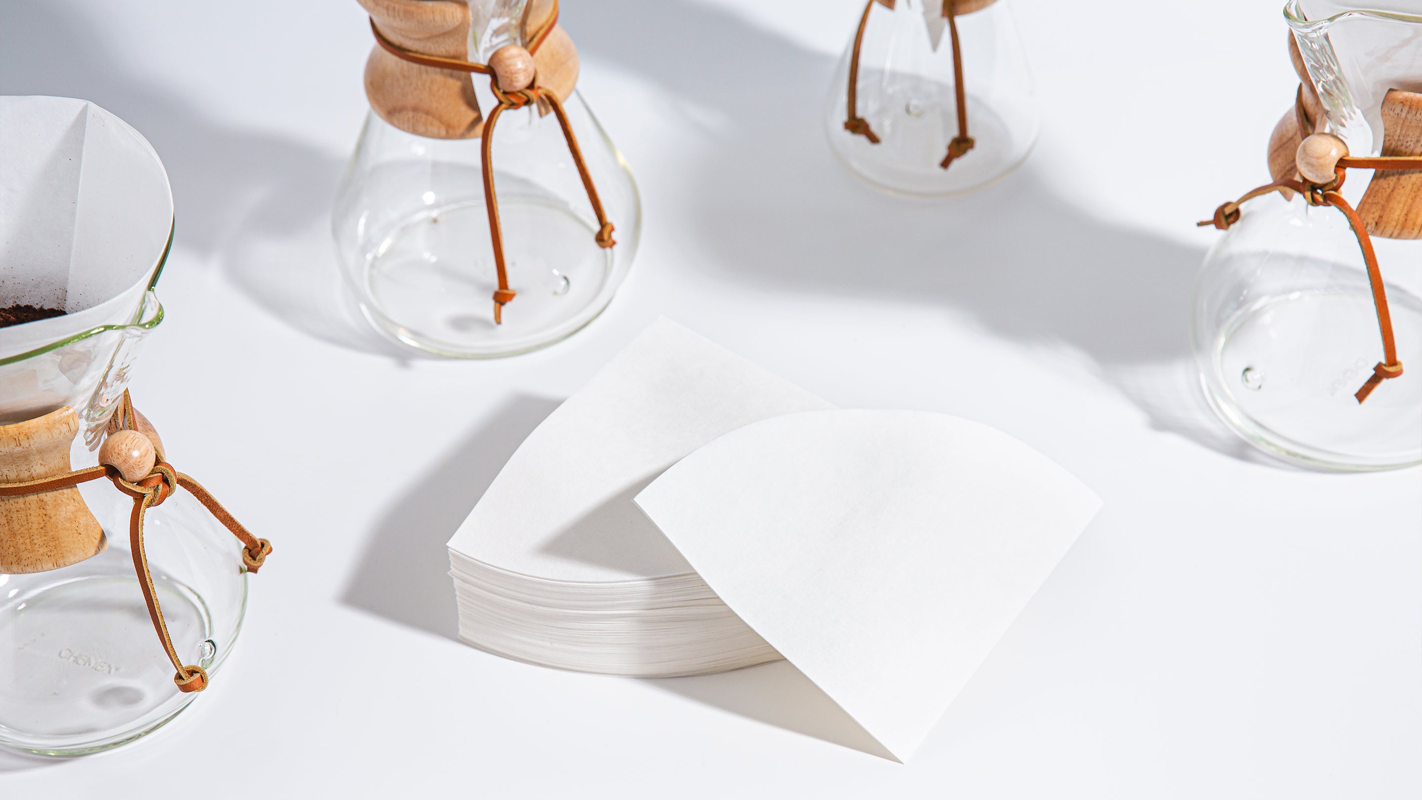 stack of white circle filters, surrounded by different size coffeemakers 