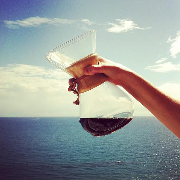 holding a chemex to the horizon line of the ocean 

