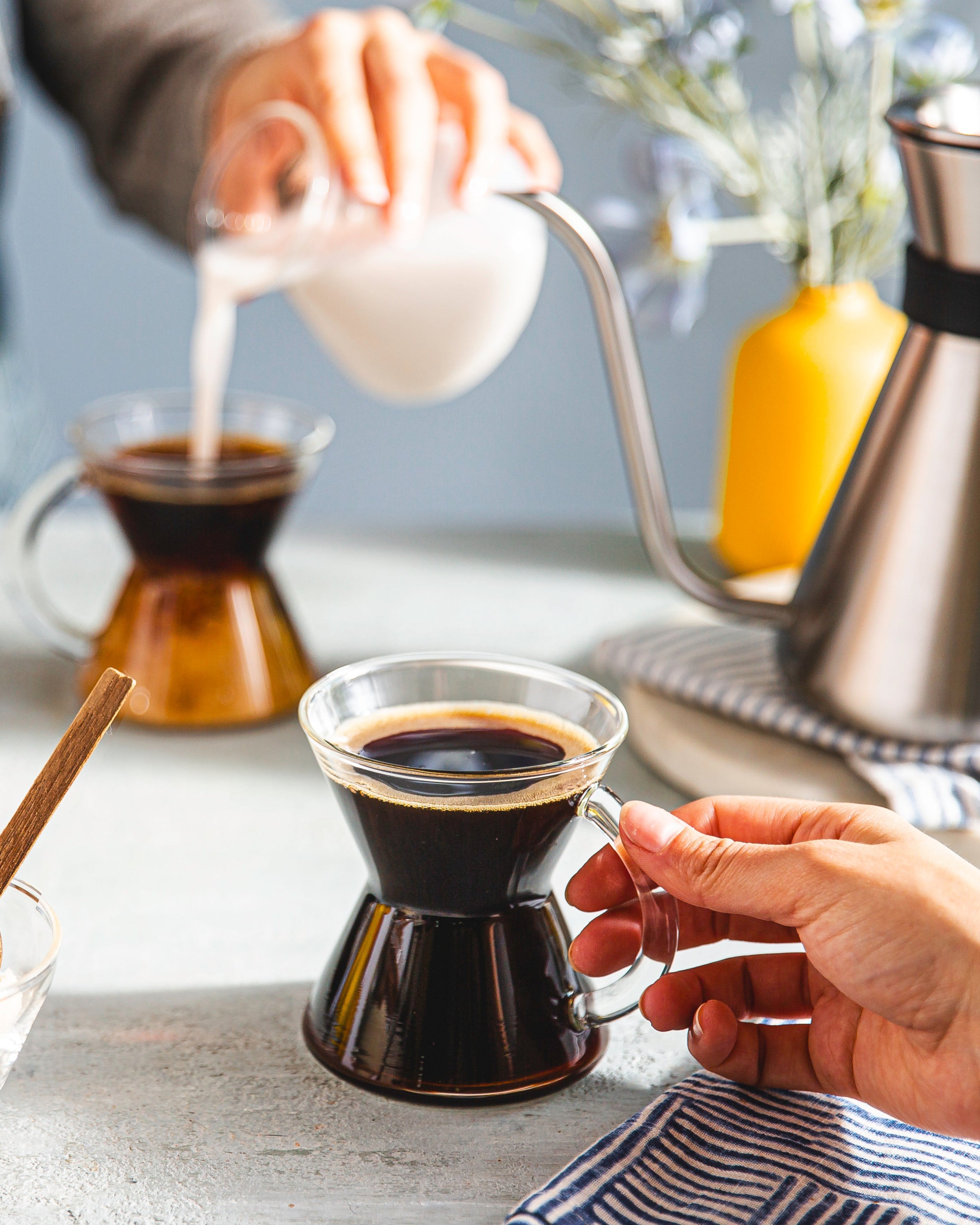 drinking coffee from a chemex coffee mug, someone pouring creamer into their coffee. 