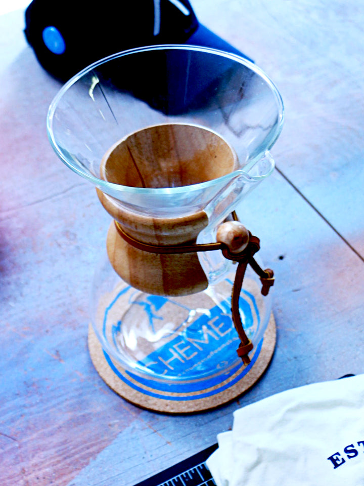 Chemex cork coaster on a wooden table with a chemex classic coffeemaker sitting on it 