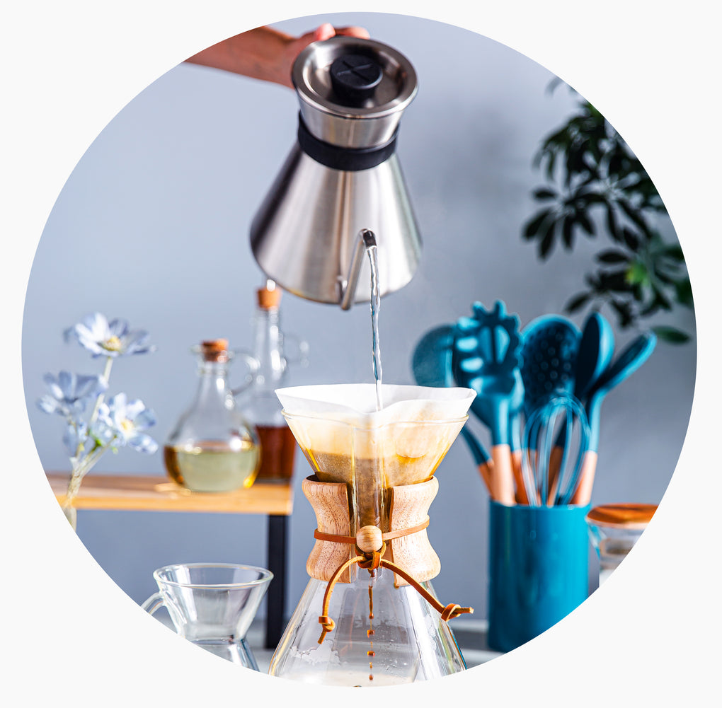 Person making coffee using a Chemex filter on a kitchen counter.