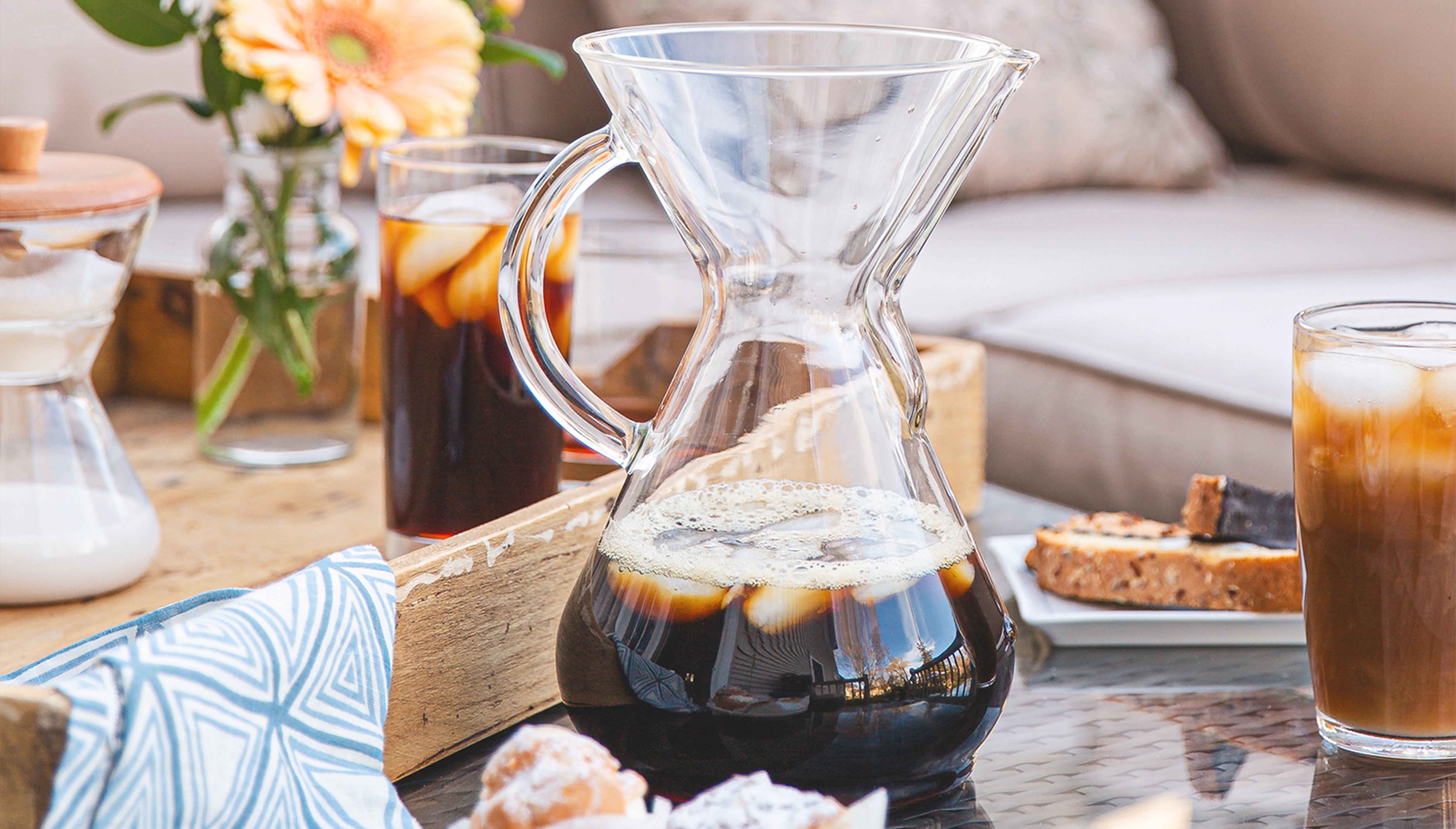 glass handle coffeemaker with iced coffee on a patio table with flowers and pastries