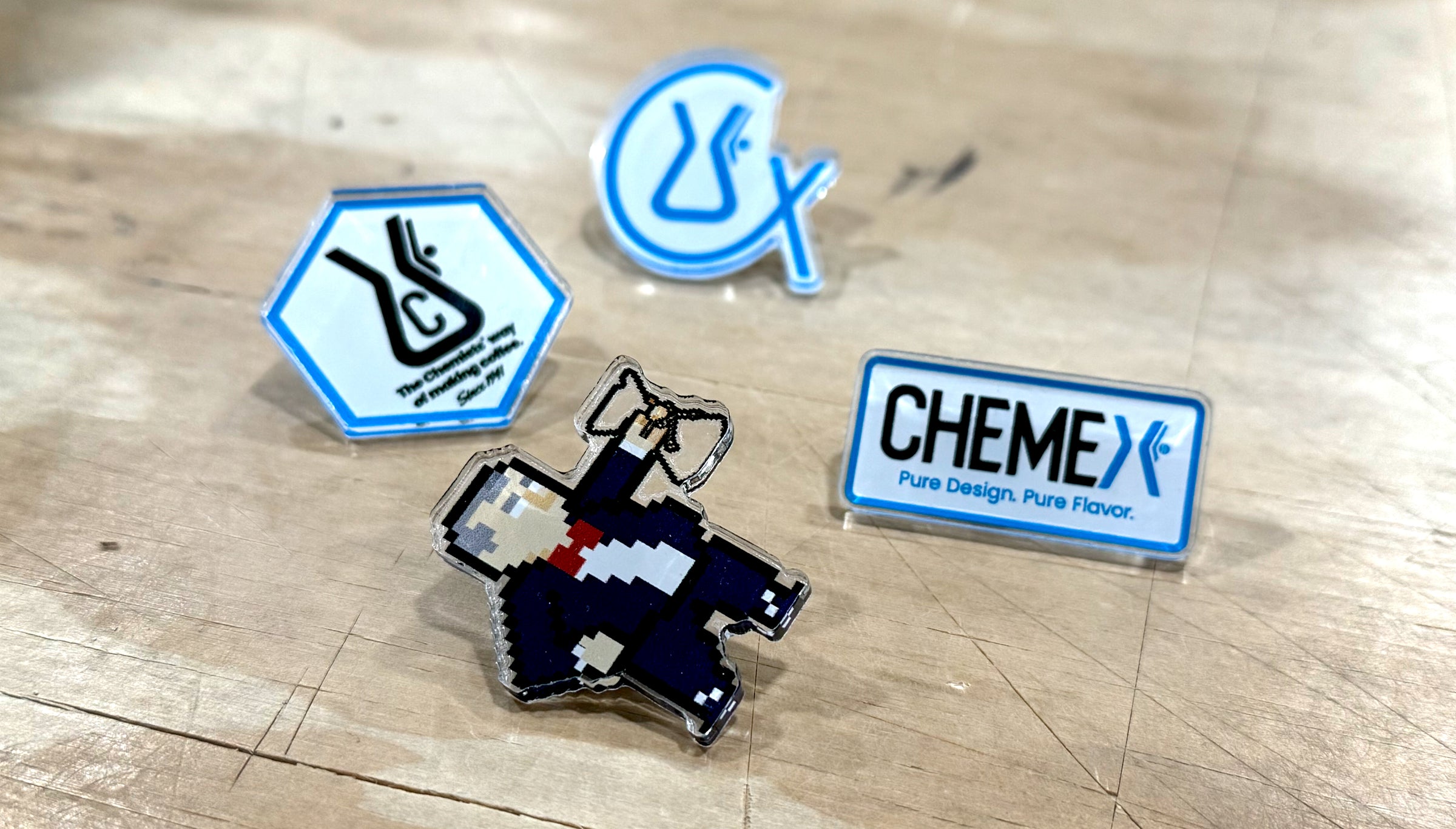 Collection of Chemex branded acrylic pins on a wooden surface