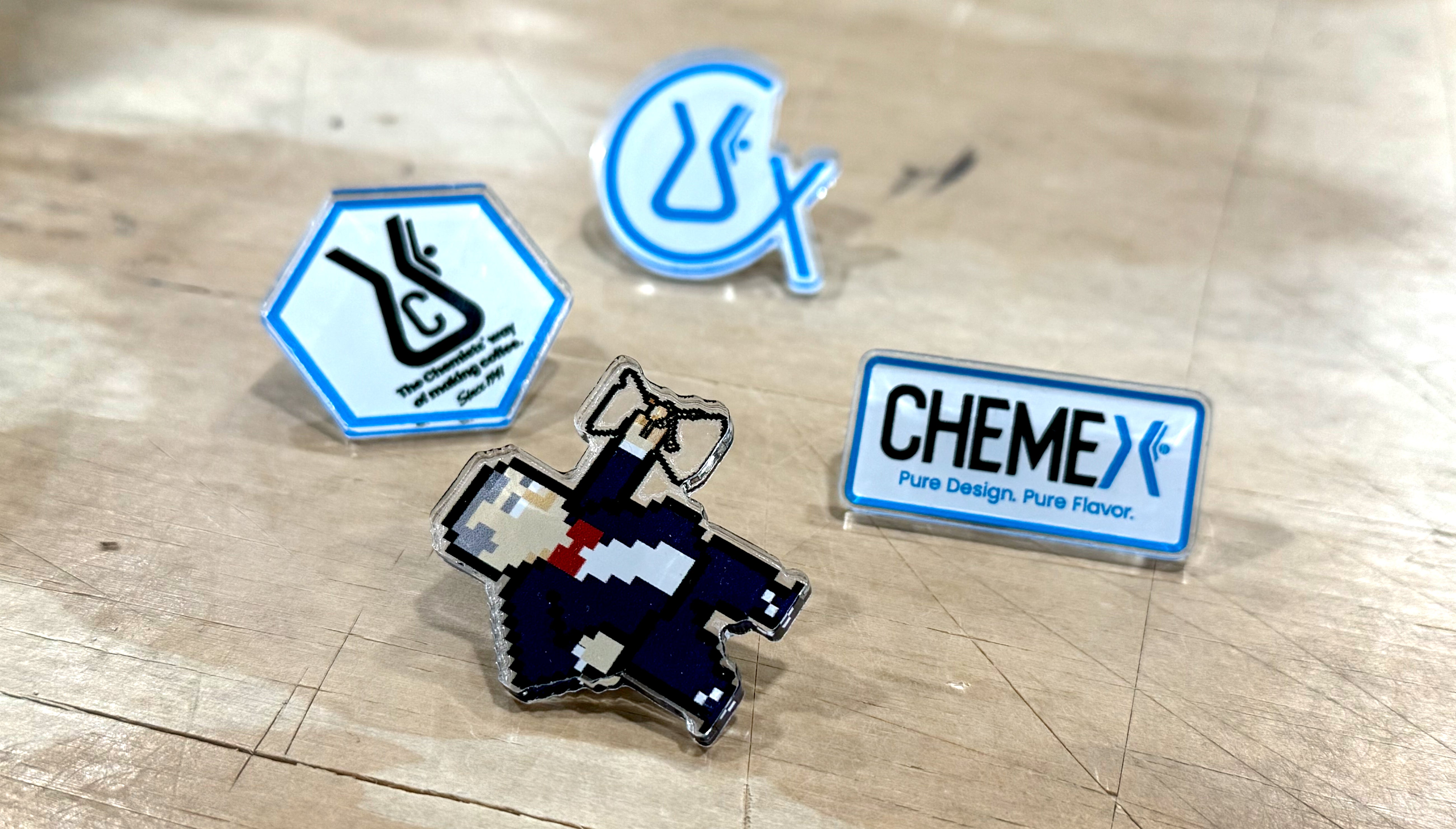 Collection of Chemex branded acrylic pins on a wooden surface