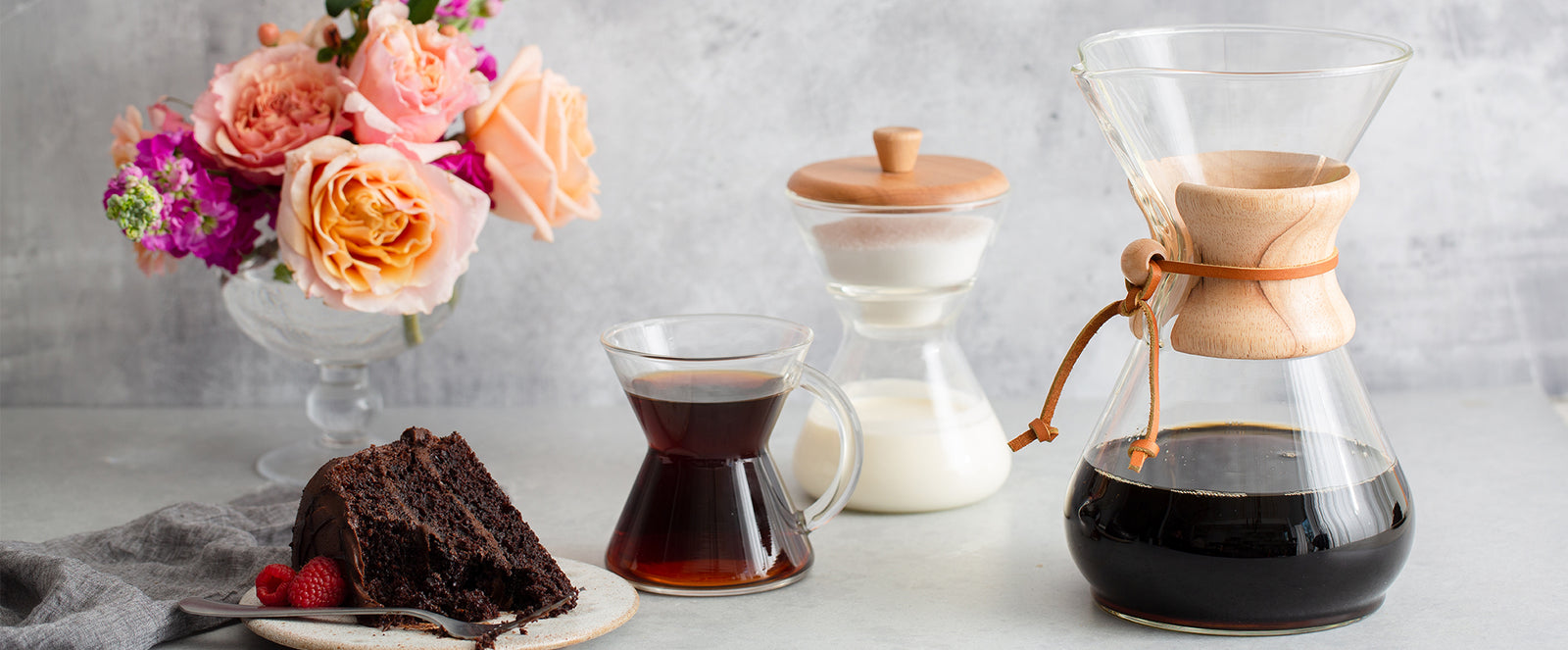 Classic coffeemaker, glass handle mug, and cream and sugar set with chocolate cake