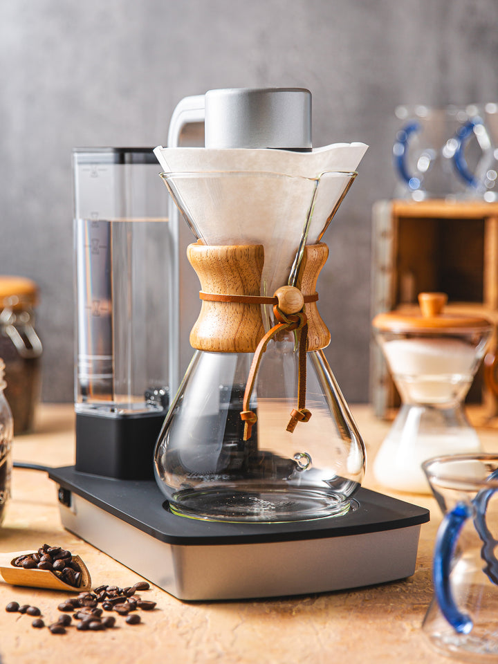 Ottomatic 2.0 on a table with a chemex circle filter. in the background there are chemex sapphire glass handle mugs and a cream and sugar set