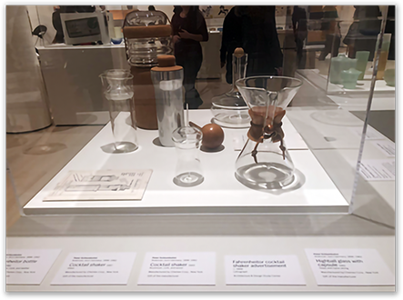 Chemex coffeemaker displayed at MoMA's Good Design Exhibition, 2019 — museum vitrine featuring cocktail shaker, decanter, glassware, and the Chemex brewer alongside design artifact placards