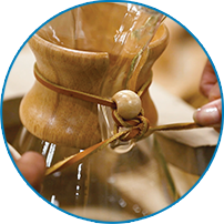Hands tying the wooden bead onto the rawhide collar of a Chemex coffeemaker, 2026